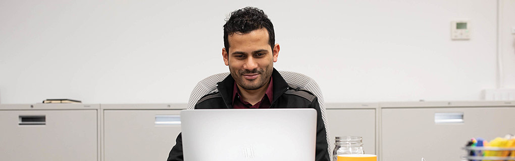 On-Ramps search analyst Saad Qureshi works on his laptop while seated at a desk.