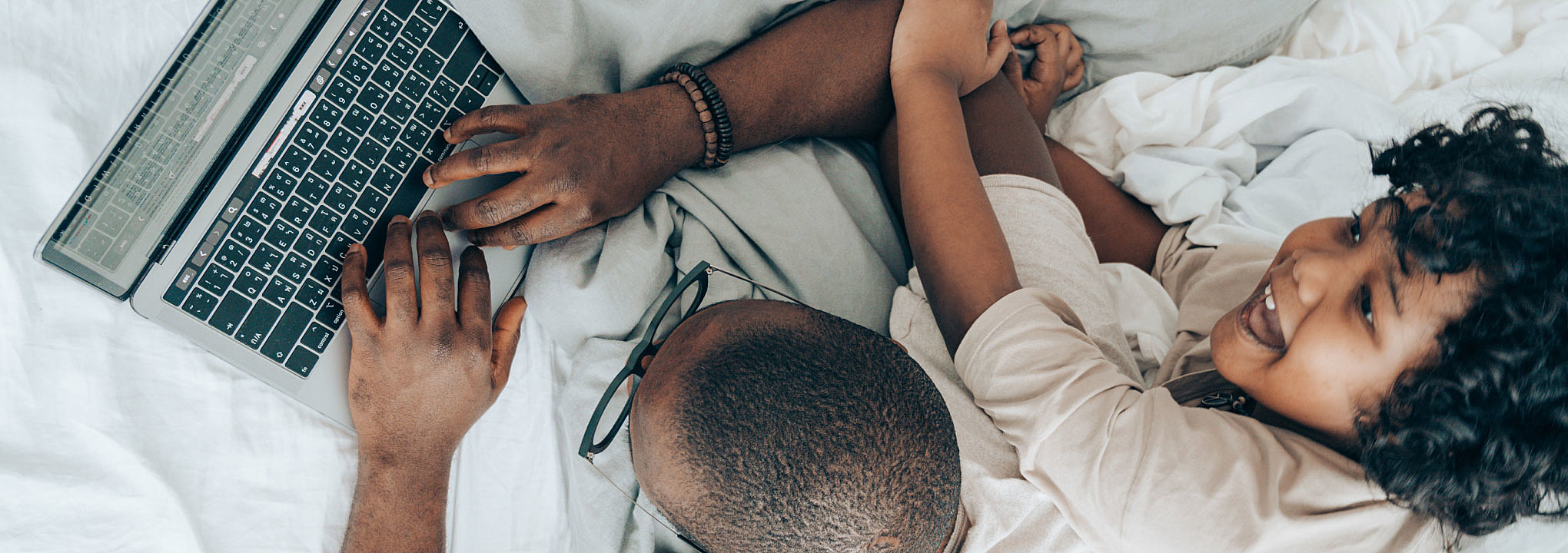 A father and daughter playfully scroll through a laptop together.