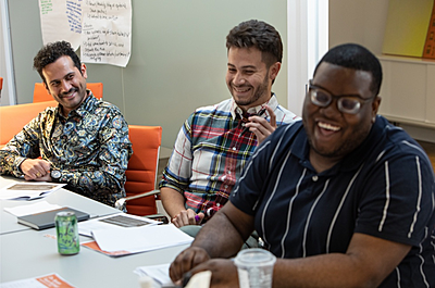 Three members of the On-Ramps team sit at a conference table smiling and laughing.