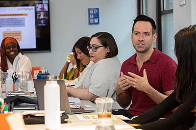 On-Rampers sit around a conference table with a Zoom presentation in the background. One On-Ramper is mid sentence with others listening intently.