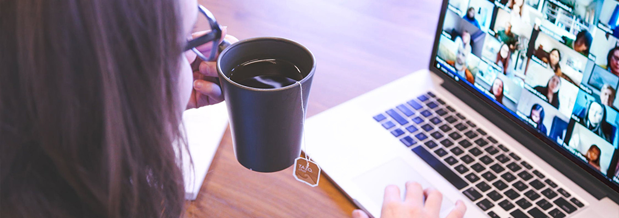 Woman holds cup of tea while attending a video conference call on her laptop